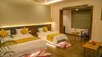 A hotel room with two beds, a small table with fruit, a chair, and a view of the outside.