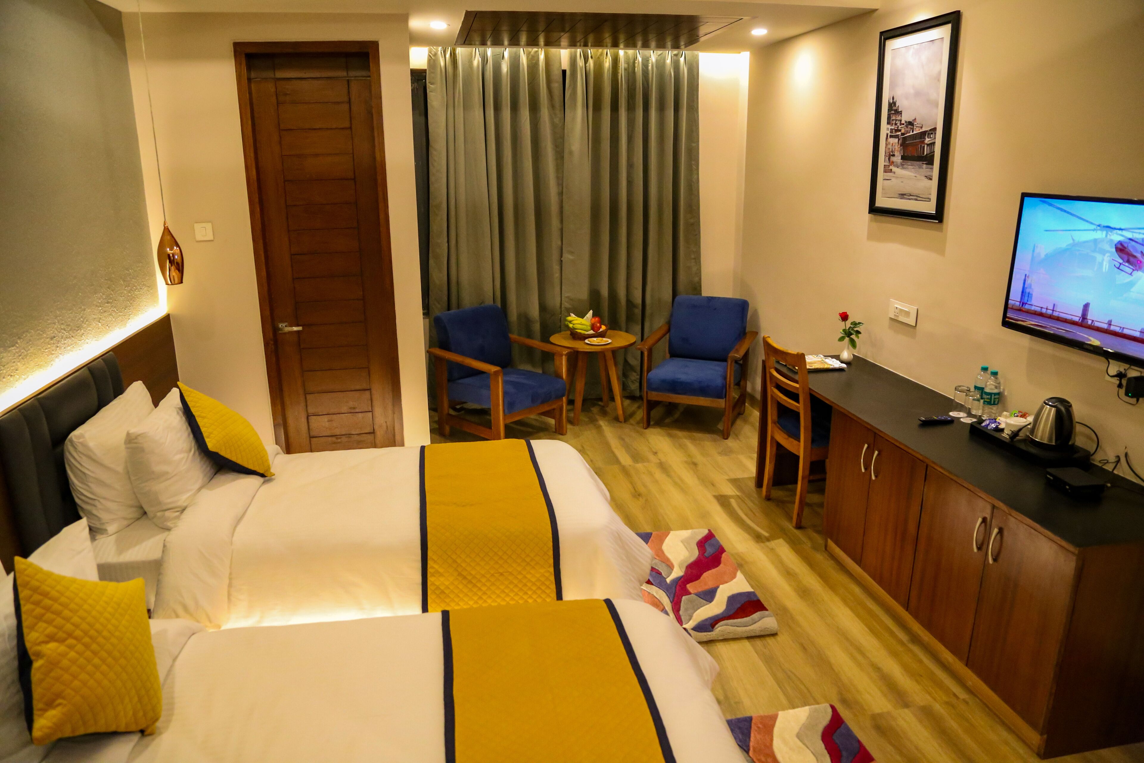 A hotel room with two beds, a desk, a chair, a television, and a curtain.