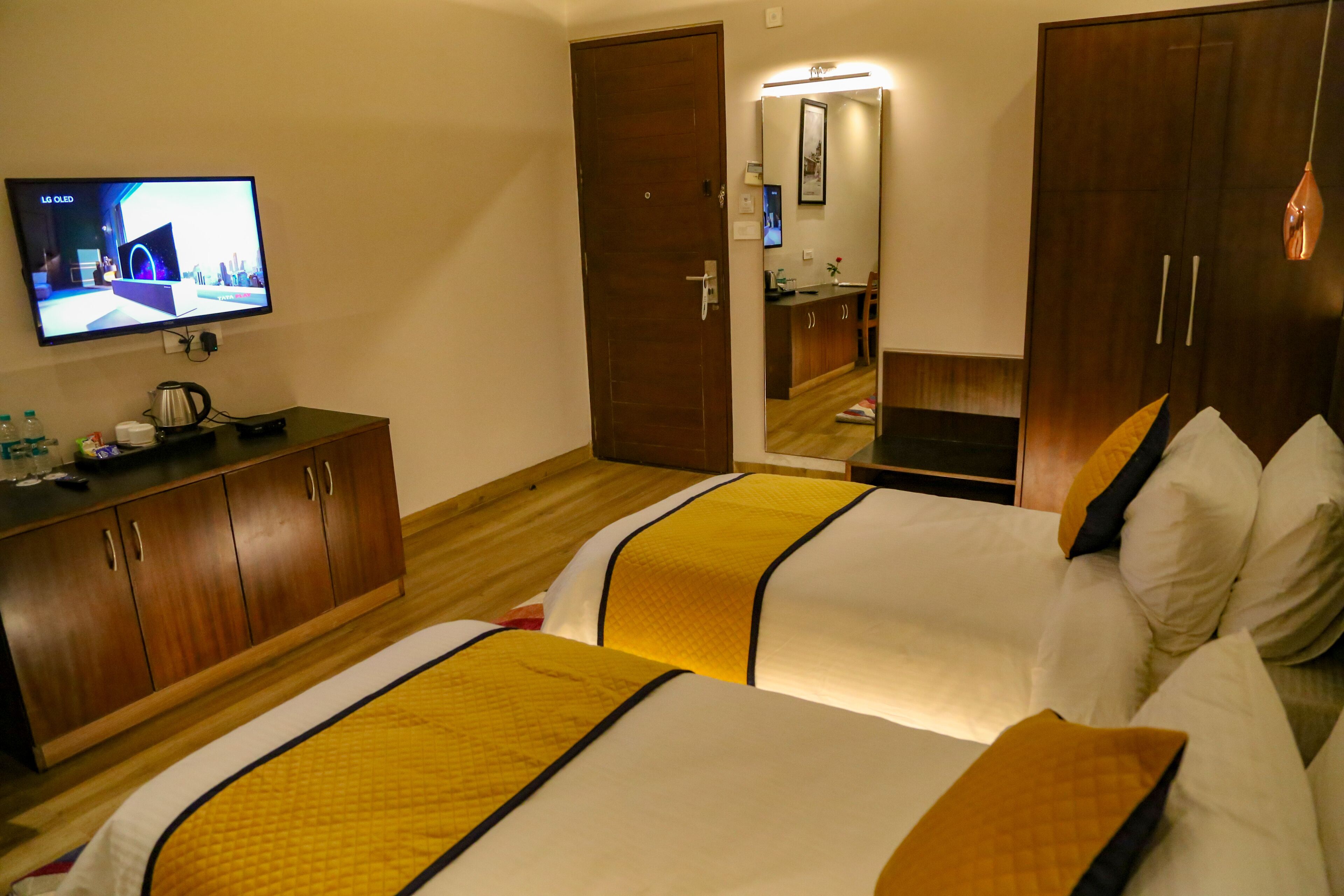 Une chambre d’hôtel avec deux lits, une télévision, des meubles en bois et une salle de bain visible à travers une porte ouverte.