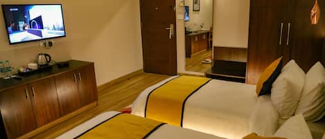 Une chambre d’hôtel avec deux lits, une télévision, des meubles en bois et une salle de bain visible à travers une porte ouverte.