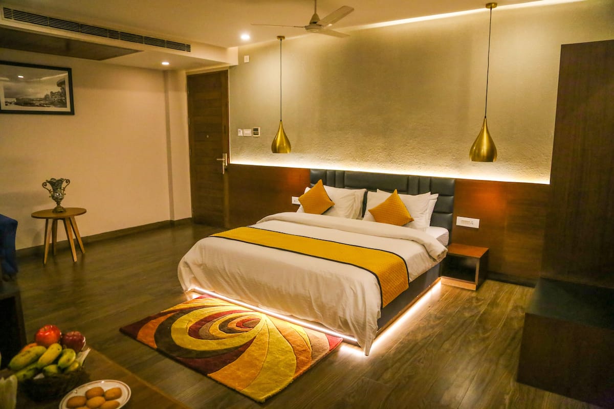 Una habitación de hotel moderna con una cama grande, mesitas de noche, un ventilador de techo y una cesta de frutas en el suelo.