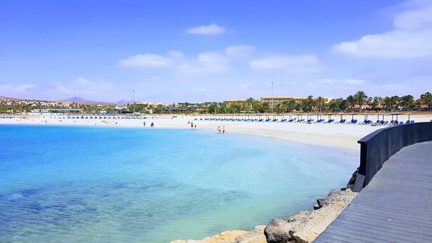 A beach with clear blue water, a sandy shore, and a wooden boardwalk.