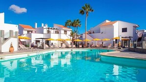 A swimming pool with sun loungers and umbrellas, surrounded by white buildings with red roofs.