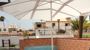 A patio area with a round table and four orange chairs, a white umbrella, and a blue cushioned bench.
