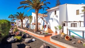 A white building with a red-tiled roof, palm trees, and a gravel pathway.