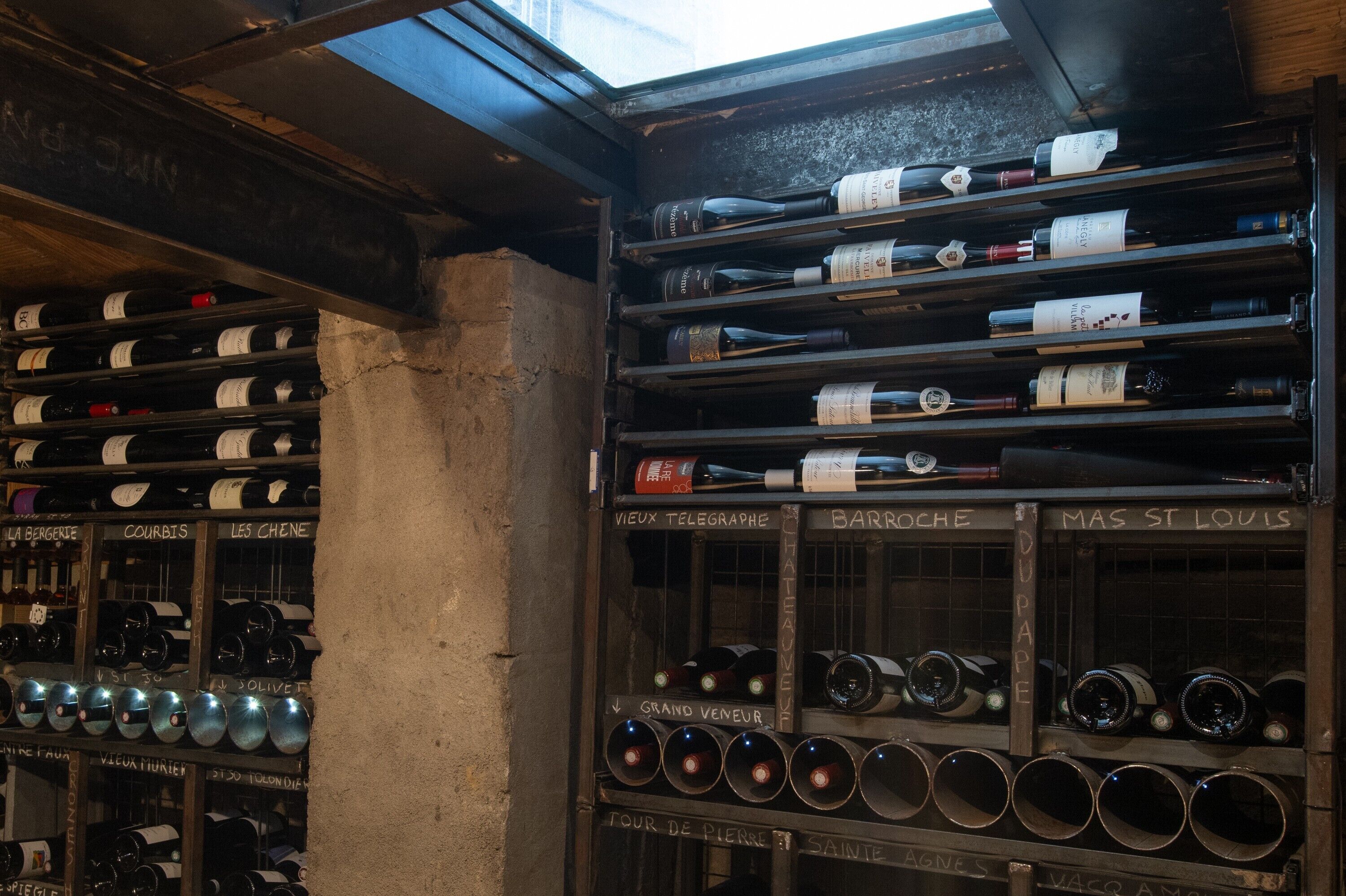Een wijnkelder met rekken voorzien van namen zoals 'Grand Vigneron' en 'Tour de Pierre'.