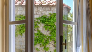 Un muro de piedra con follaje verde, techo de tejas y una ventana con cortina.