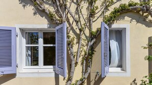Un edificio con dos ventanas, una con contraventanas abiertas y la otra cerrada.
