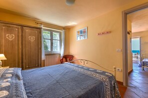 A bedroom with a bed, a chair, a wardrobe, a window, and a door leading to a balcony.