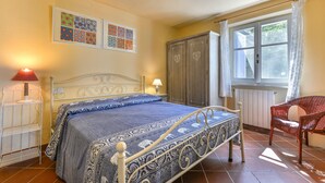 Un dormitorio con cama, una silla, un armario y una ventana con cortinas.