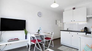 A modern kitchen with white cabinets, a dining area with white chairs, a flat-screen TV, and a clock on the wall.