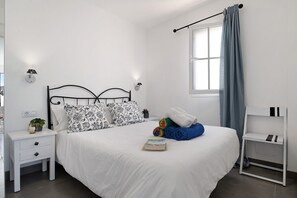 Une chambre à coucher bien rangée, avec un lit, des tables de chevet, une commode, une lampe et une fenêtre avec des rideaux.