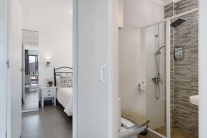 Une salle de bain moderne équipée d’une douche, de toilettes et d’une table de chevet avec une lampe.