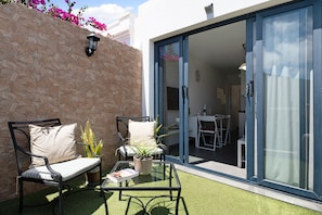 Une terrasse avec un mur en pierre, une porte vitrée donnant sur un espace intérieur et une petite table agrémentée d’une plante.