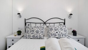 A bed with a white sheet, two black and white patterned pillows, a black metal headboard, two bedside tables with lamps, and a small potted plant on one table.