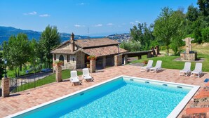 A pool with lounge chairs, a stone building, and a view of the landscape. - Villa San Martino (Torgiano)