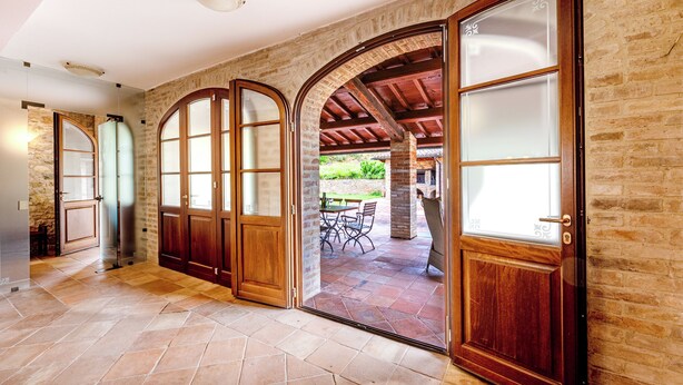 A spacious hallway with arched wooden doors leading to an outdoor patio area. - Villa San Martino (Torgiano)