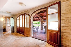 A spacious hallway with arched wooden doors leading to an outdoor patio area. - Villa San Martino (Torgiano)