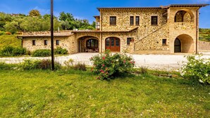 A stone house with a tiled roof, arched doorways, and a small garden with pink flowers. - Villa San Martino (Torgiano)