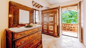 A wooden dresser with drawers and a mirror, a door with a stone wall outside, and a tiled floor. - Villa San Martino (Torgiano)