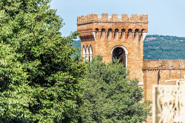 Ein historischer Backsteinturm mit rundbogigen Fenstern und Zinnen, umgeben von üppigem Grün.