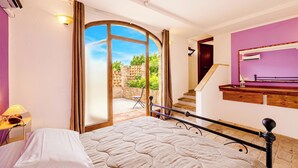 A bedroom with a bed, a nightstand, a lamp, a window with curtains, a staircase, and a bathroom with a mirror. - Villa San Martino (Torgiano)