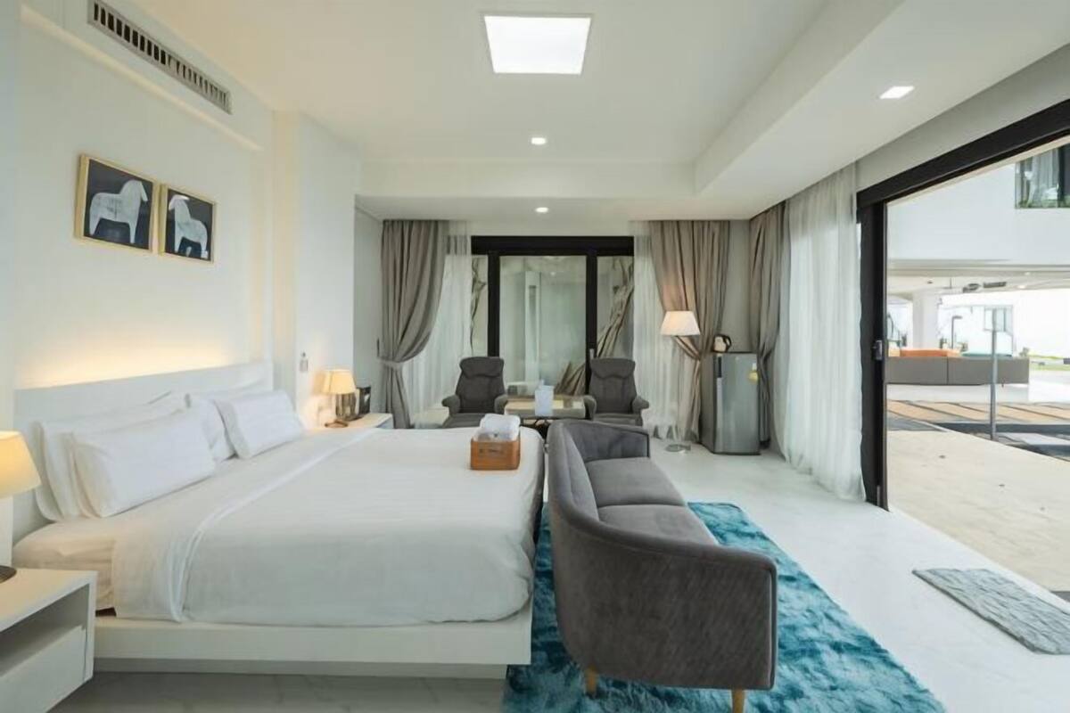 A modern hotel room with a large bed, a sofa, a desk, and a view of the outside.