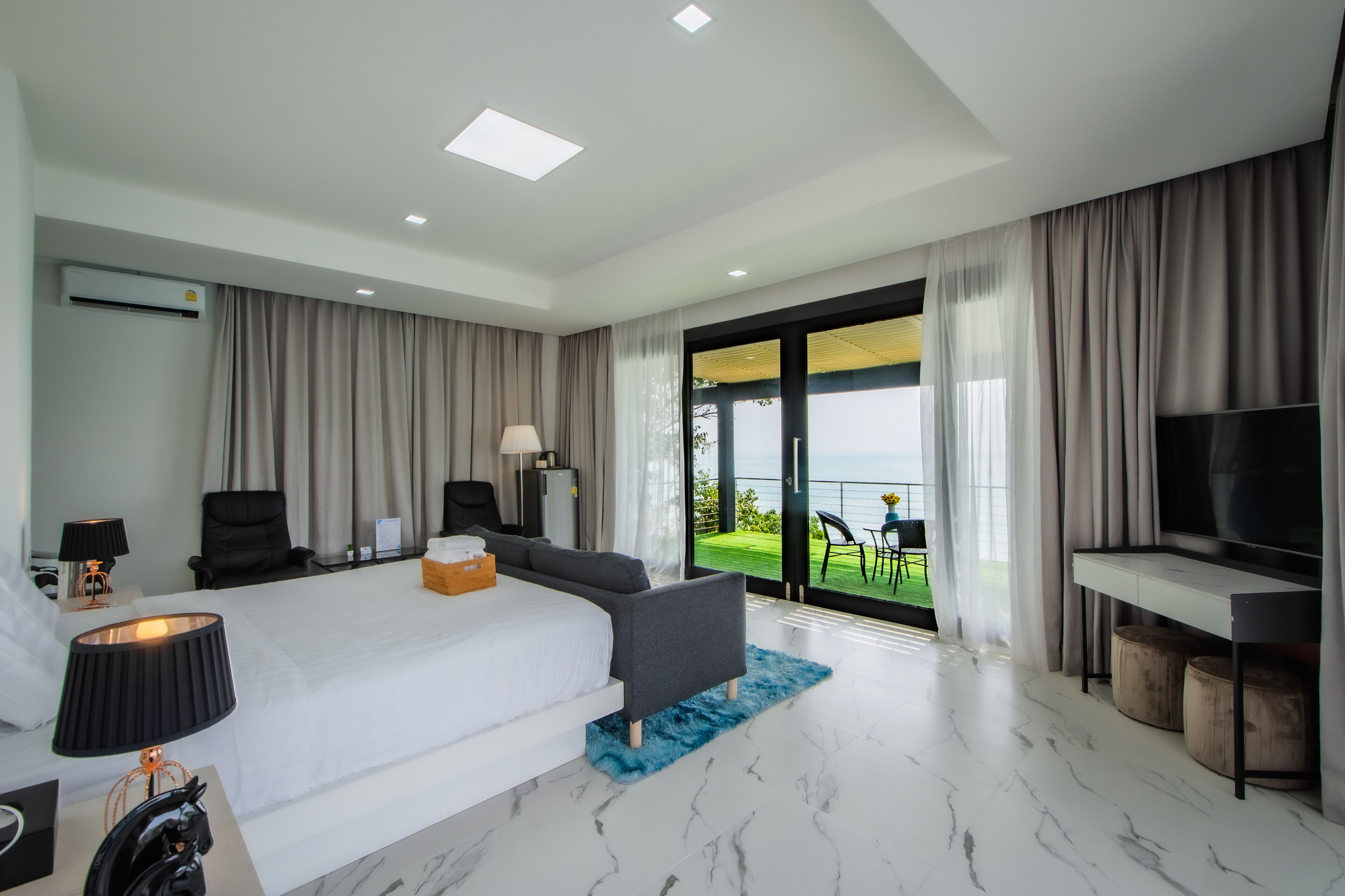 A modern hotel room with a large bed, a TV, a desk, and a balcony with a view.