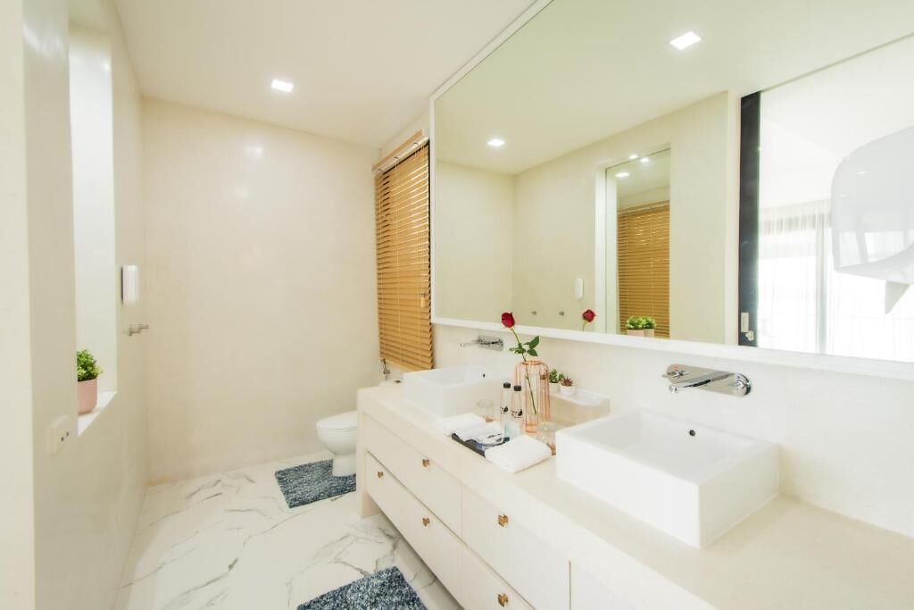 A modern bathroom with a white vanity, two sinks, a large mirror, and a toilet.