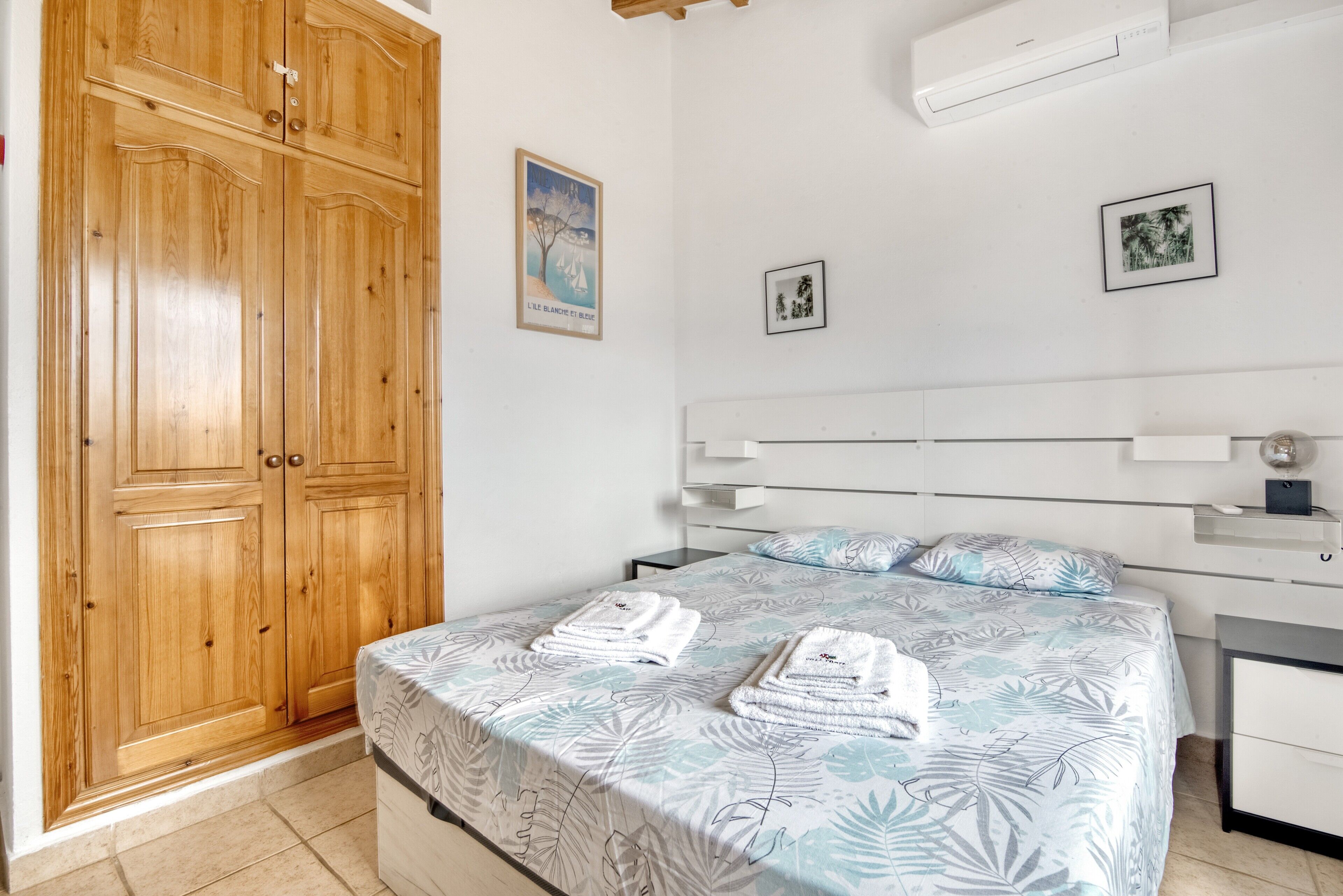 Un dormitorio con cama, armario de madera y estantes en la pared.