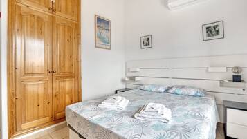 Un dormitorio con cama, armario de madera y estantes en la pared.