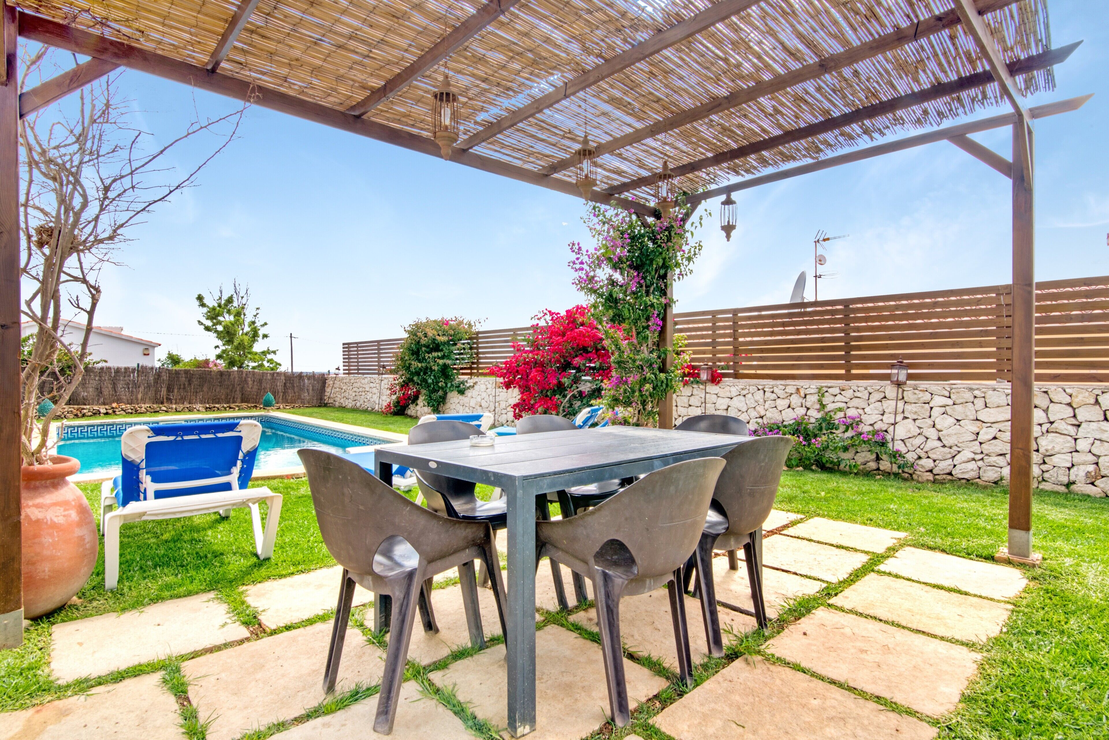 Eine Terrasse im Freien mit Tisch und Stühlen, einem Pool und einer Pergola.