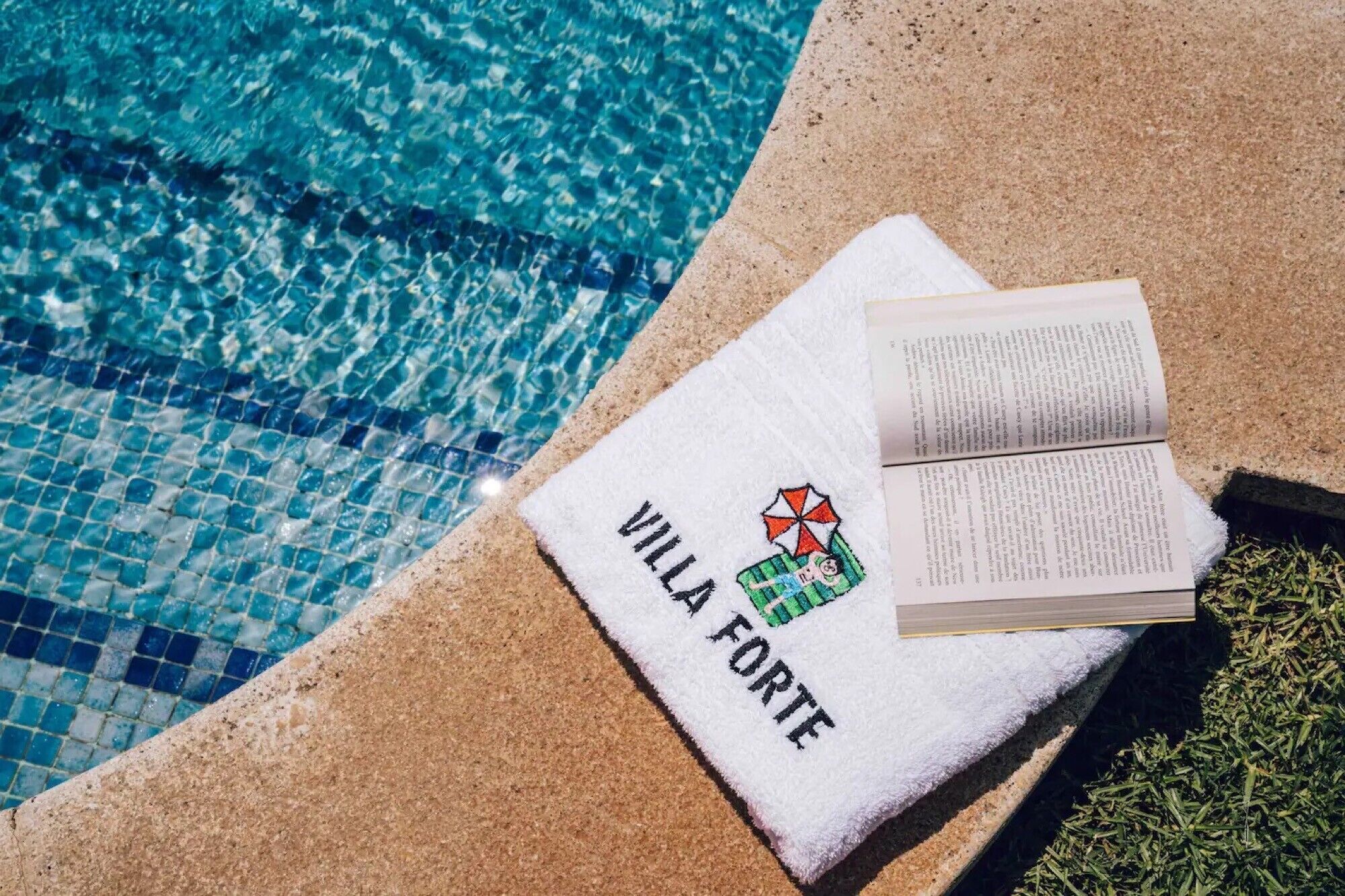 A poolside towel with 'VILLA FORTE' printed on it, a book, and a small decorative item.