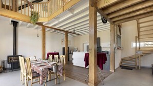 A spacious dining area with wooden chairs and a table set for a meal, a staircase, and a kitchen area in the background.
