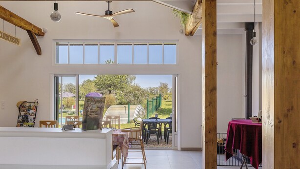 A spacious room with a high ceiling, large windows, a dining area with chairs and a table, and a view of the outdoors.