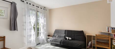 Un dormitorio con una cama, un sofá, una silla de madera, una mesita y una estantería.