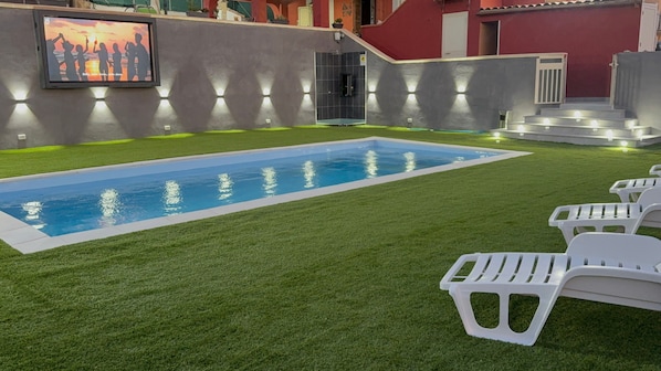 Una piscina con césped artificial, sillas de plástico blancas y un cuadro colgado en la pared.