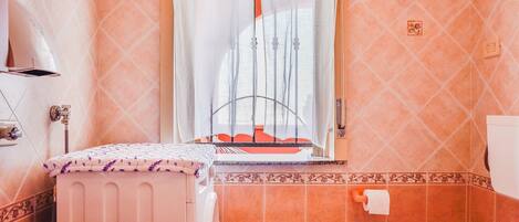 A bathroom with a window, a radiator, a toilet, and a sink.