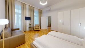 Une chambre d’hôtel moderne avec un grand lit, un canapé, un fauteuil, une petite table avec un vase et un téléviseur fixé au mur.