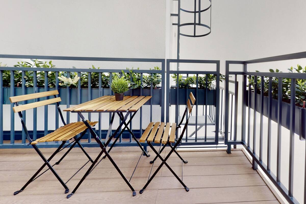 Un balcon avec une table et des chaises en bois, une plante en pot et une rambarde bleue.