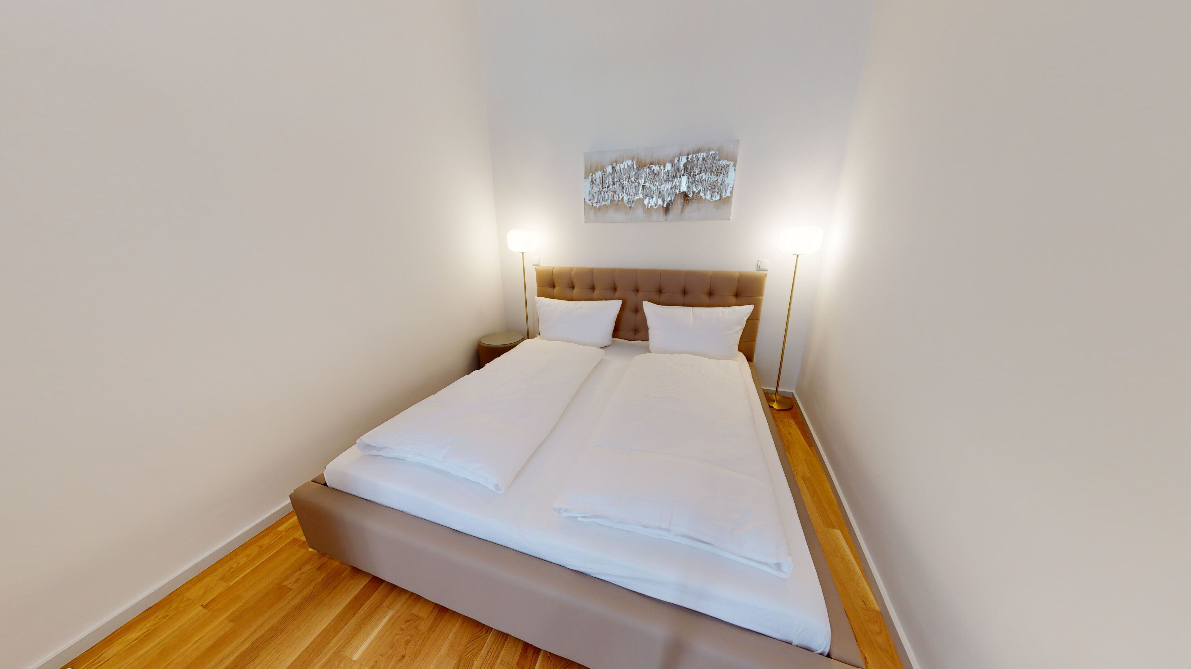 Una cama bien hecha con sábanas blancas, suelo de madera y cabecera con diseño texturizado.