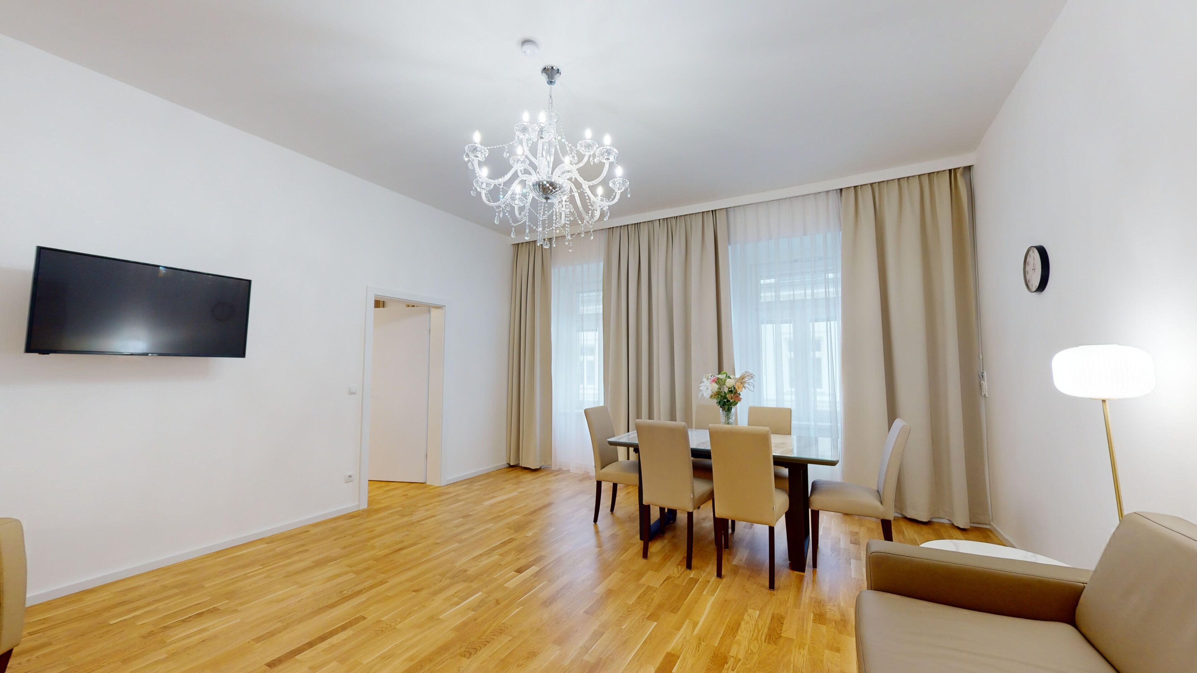 Ein modernes Wohnzimmer mit Holzboden, einem Esstisch mit Stühlen, einer Couch, einer Deckenleuchte, einem Flachbildfernseher und einer Lampe.