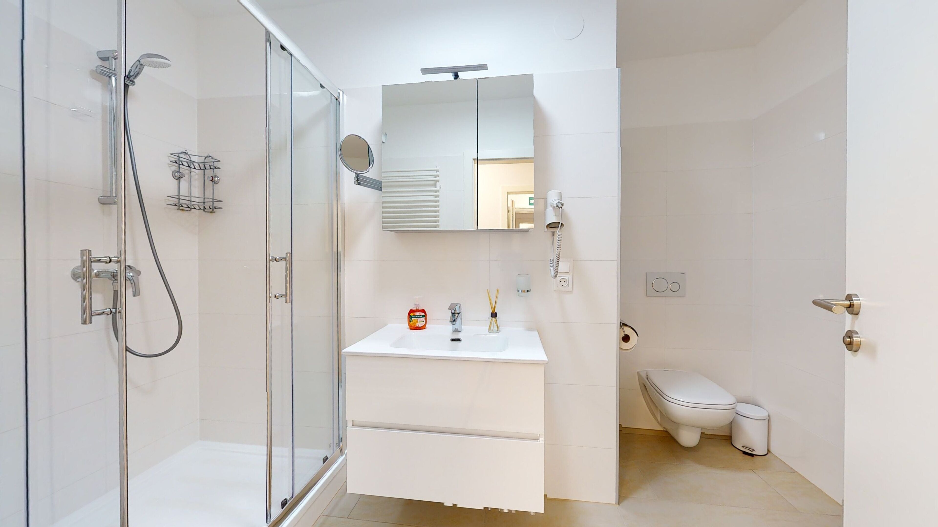 A modern bathroom with a glass-enclosed shower, a white sink with a mirror above, and a toilet.
