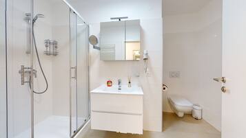 A modern bathroom with a glass-enclosed shower, a white sink with a mirror above, and a toilet.