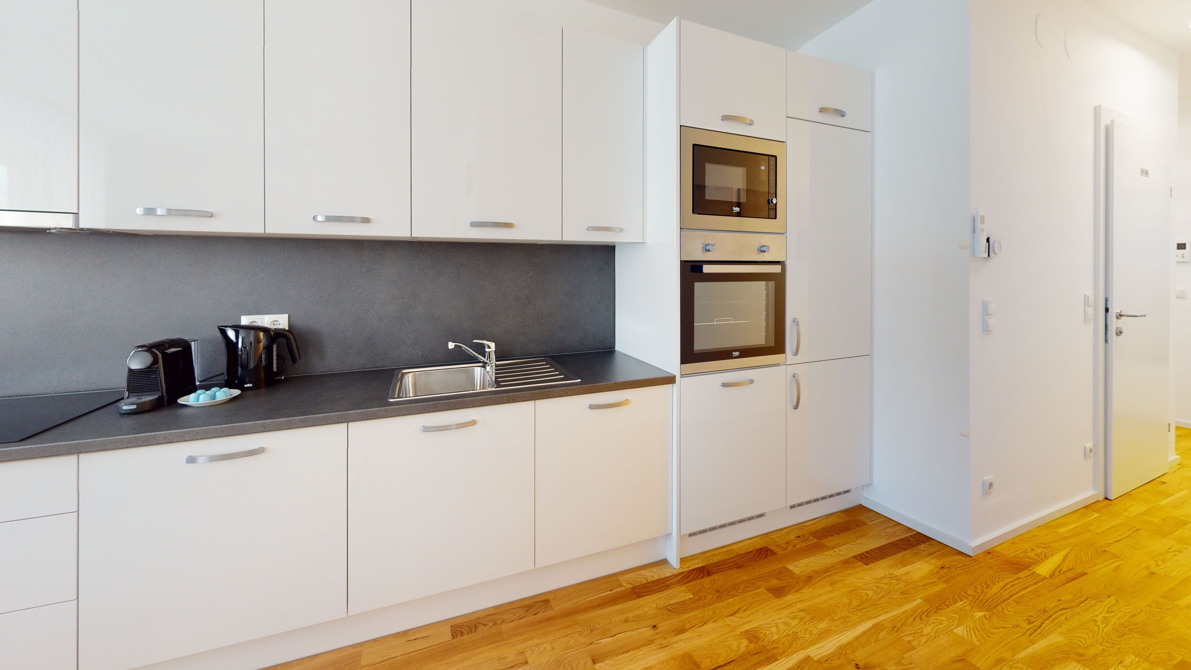 Una cocina moderna con armarios blancos, una encimera negra y un horno empotrado.