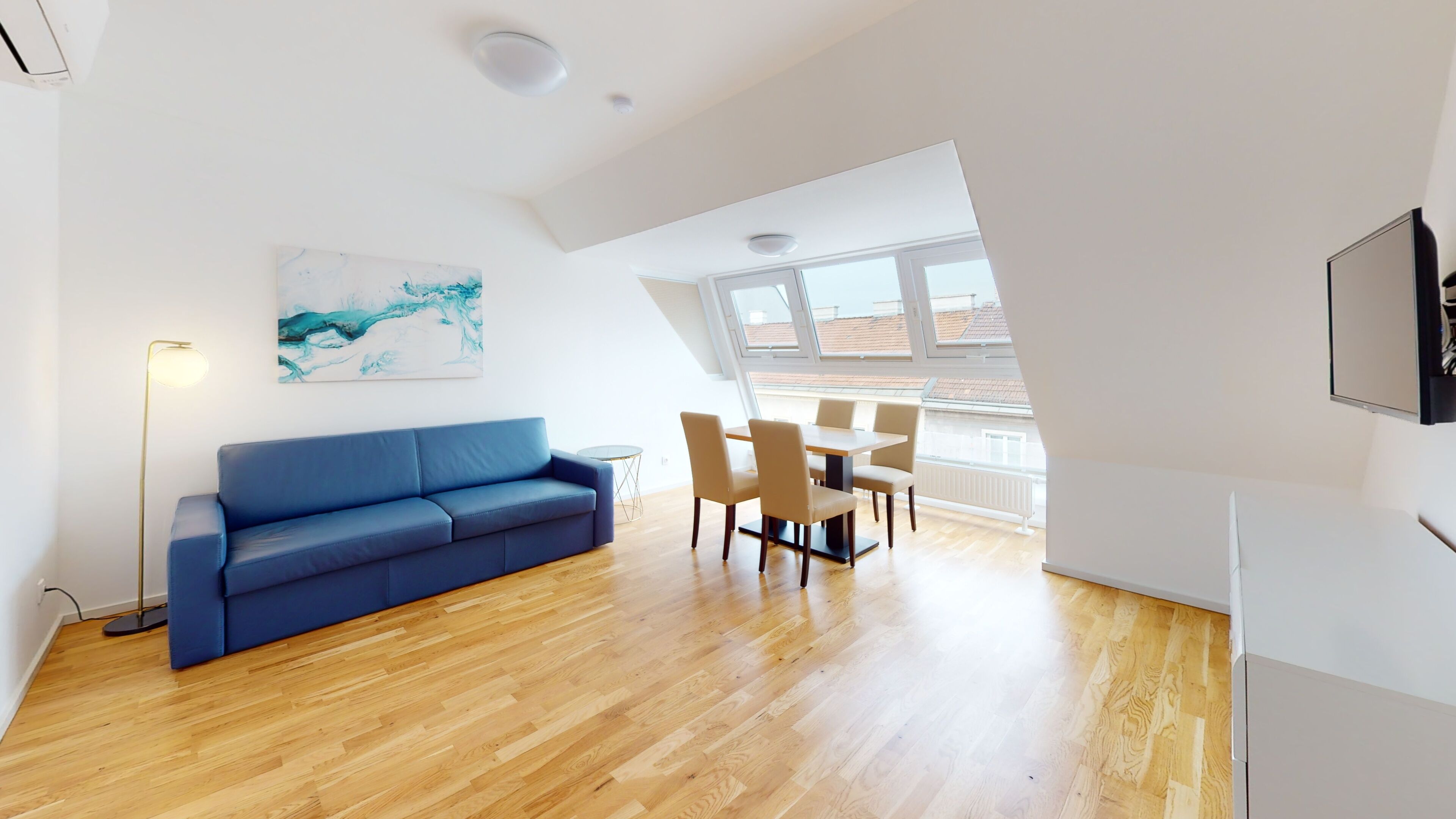 Ein modernes Wohnzimmer mit einem blauen Sofa, einem Esstisch mit Stühlen und einem großen Fenster mit Stadtblick.