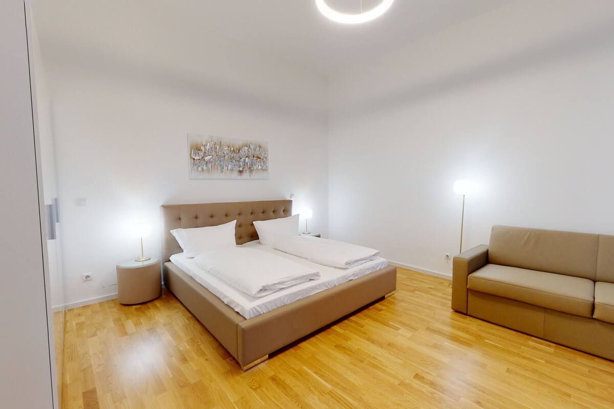 Une chambre à coucher avec un lit, des tables de chevet, une lampe, un canapé et un tableau au mur.