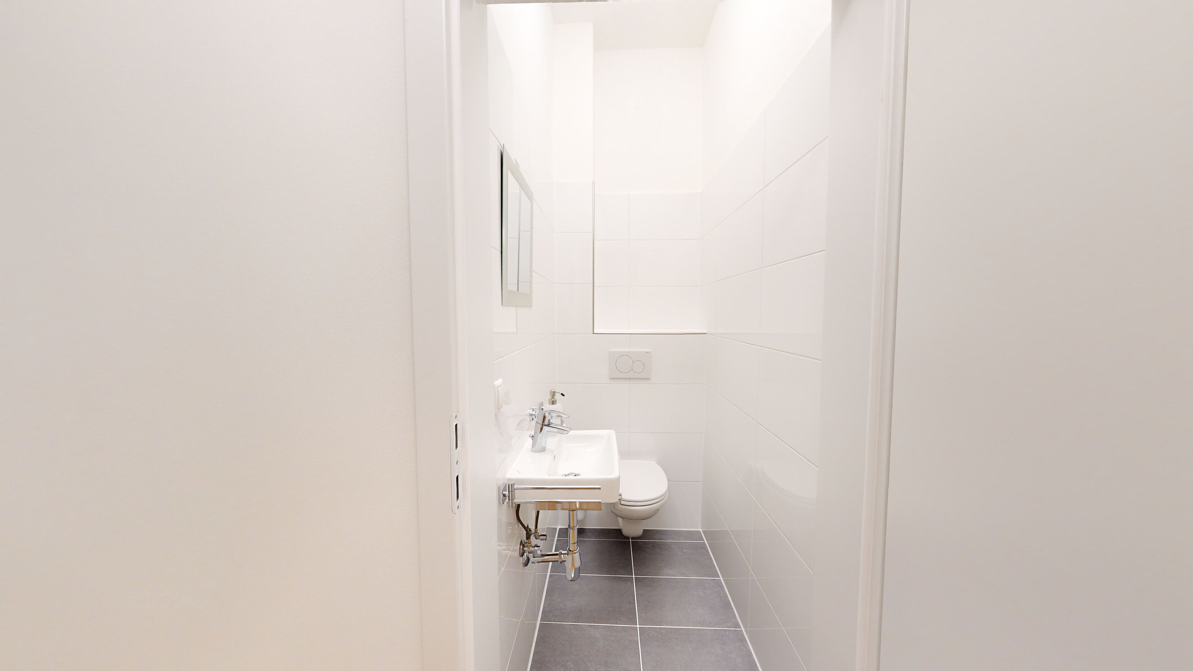 A narrow hallway leading to a bathroom with a white sink, toilet, and a mirror.