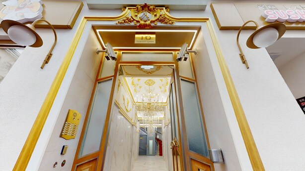 Une entrée imposante, ornée d’un lustre, avec une enseigne indiquant « Rotenstengasse 16 » et, au fond, une enseigne annonçant un restaurant de sushis.