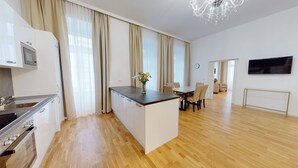Une cuisine moderne dotée d’un four encastré, un coin repas avec une table et des chaises en bois, et un salon avec une télévision et un lustre.